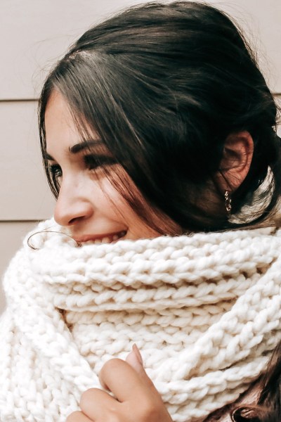 A picture of a girl wearing a cream colour crochet infinity scarf with a plain background