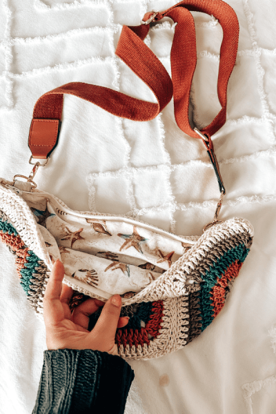 an image of a granny squares crochet bag with brow fabric straps on a white bed.