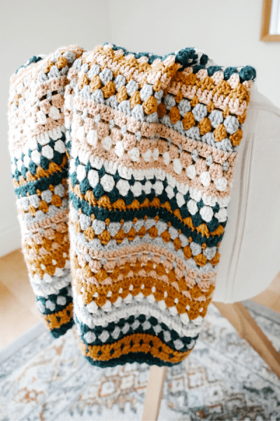a crochet baby blanket with colour stripes hanging from a chair.