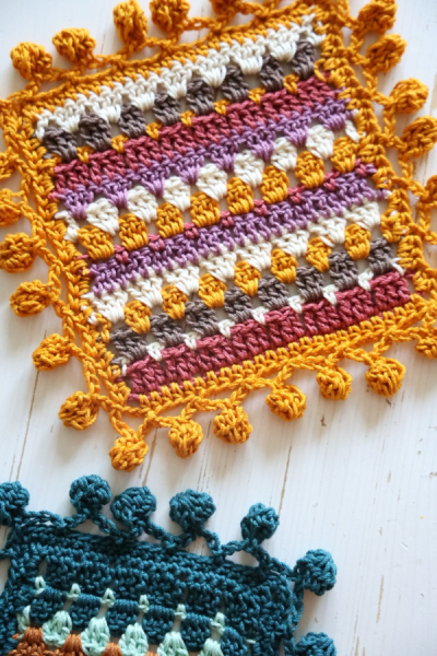 a colorful crochet coaster with pompom edging