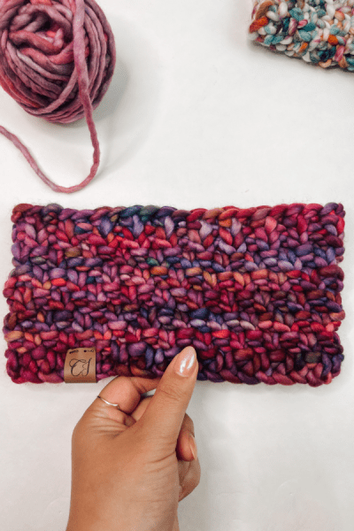 an image of a headband knitted in purple with a hand holding it